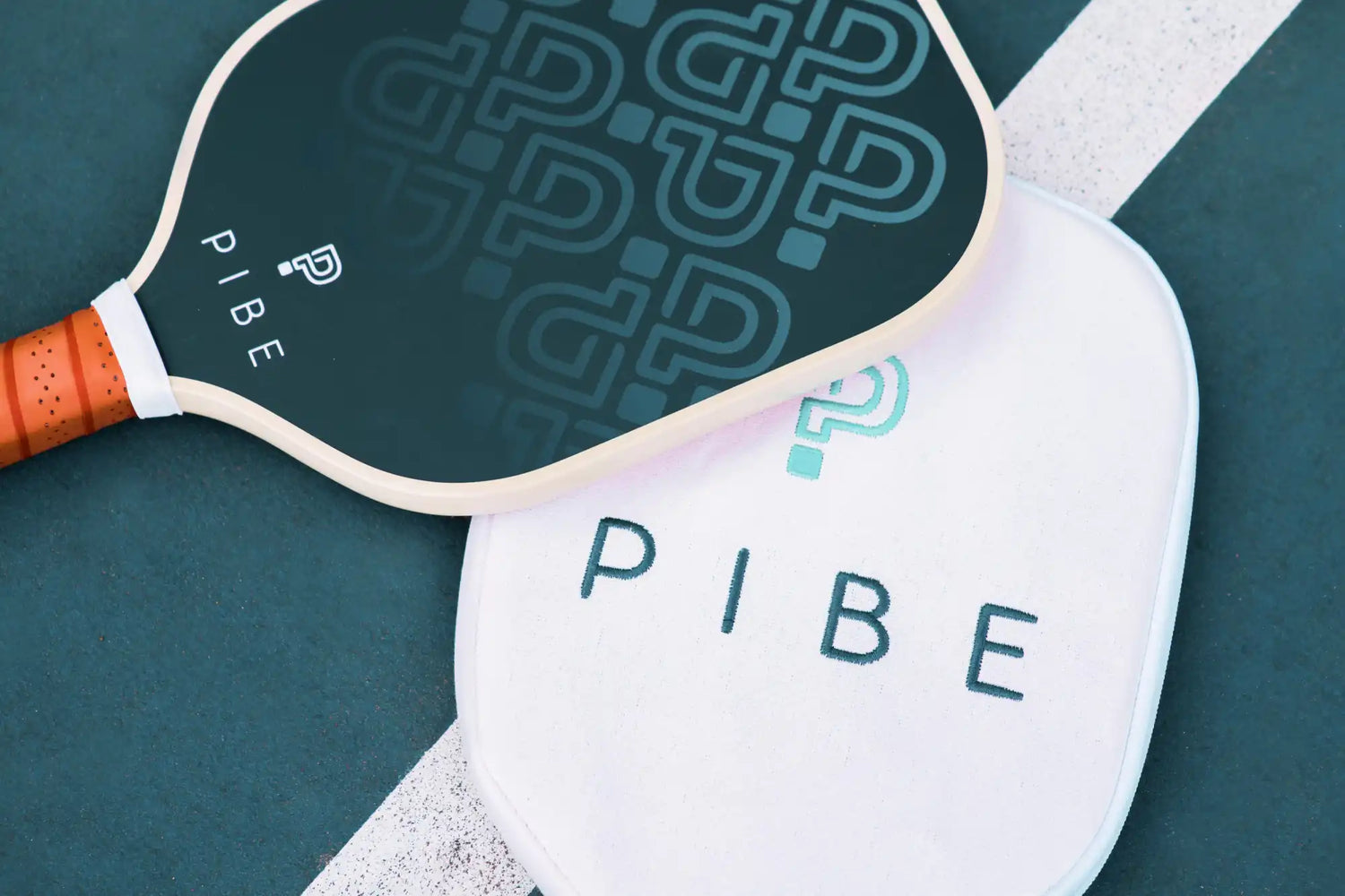 Two pickleball paddles in dark teal and white with ’PIBE’ branding.